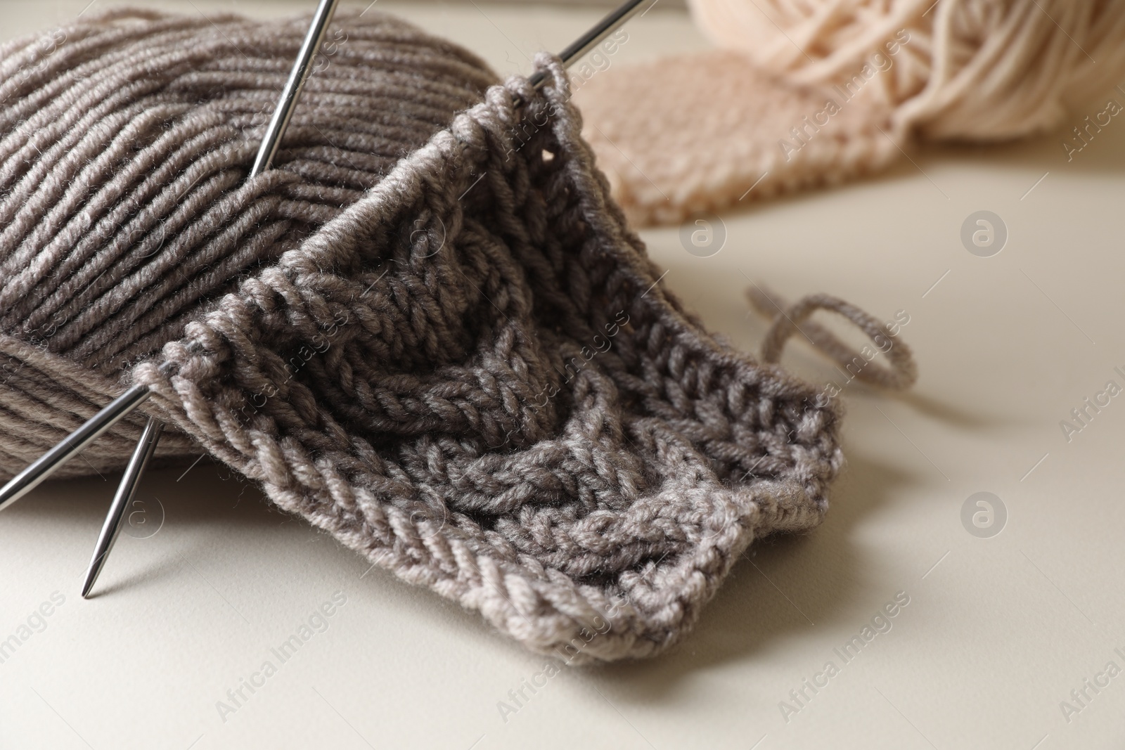 Photo of Knitting, soft yarn and needles on beige background, closeup