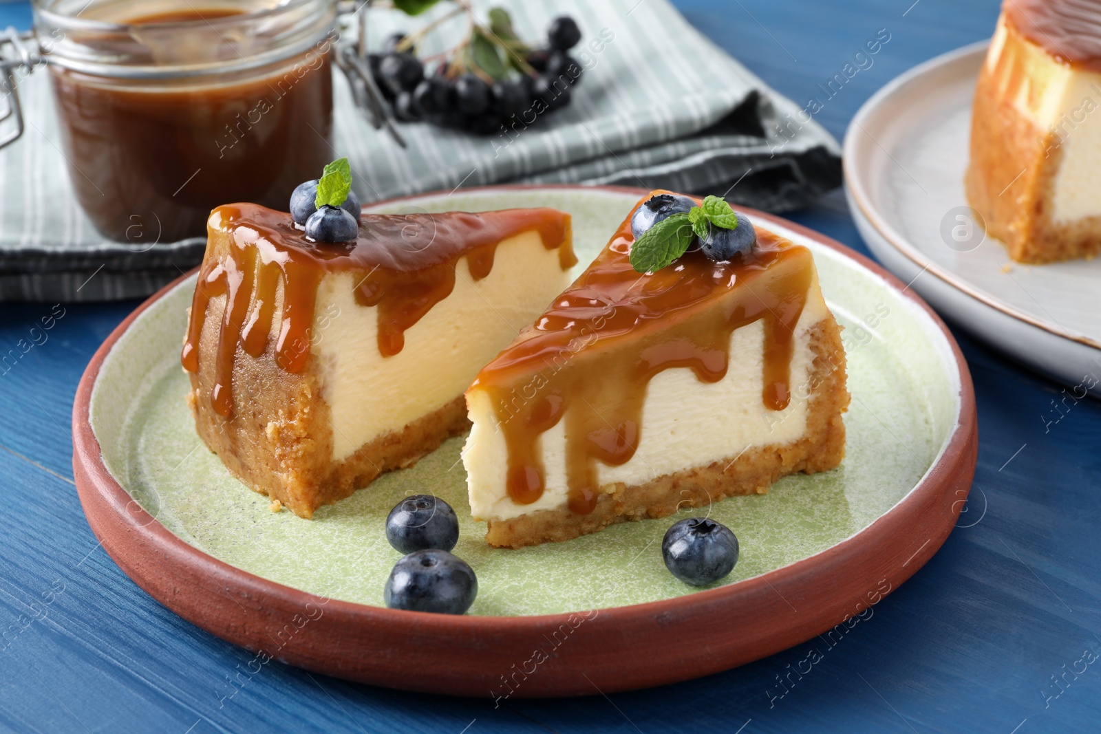 Photo of Pieces of delicious caramel cheesecake with blueberry and mint on blue wooden table