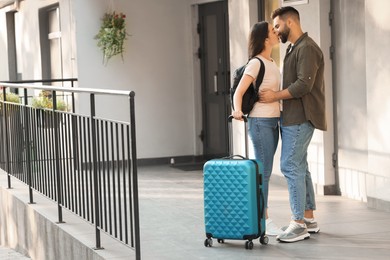 Photo of Long-distance relationship. Beautiful young couple with luggage kissing near house entrance outdoors