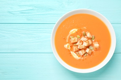 Photo of Tasty creamy pumpkin soup with croutons and seeds in bowl on light blue wooden table, top view. Space for text
