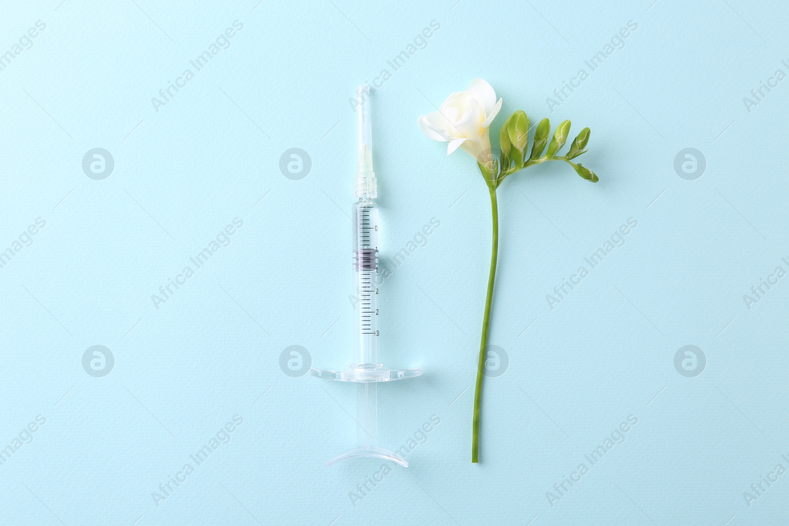 Photo of Cosmetology. Medical syringe and freesia flower on light blue background, flat lay