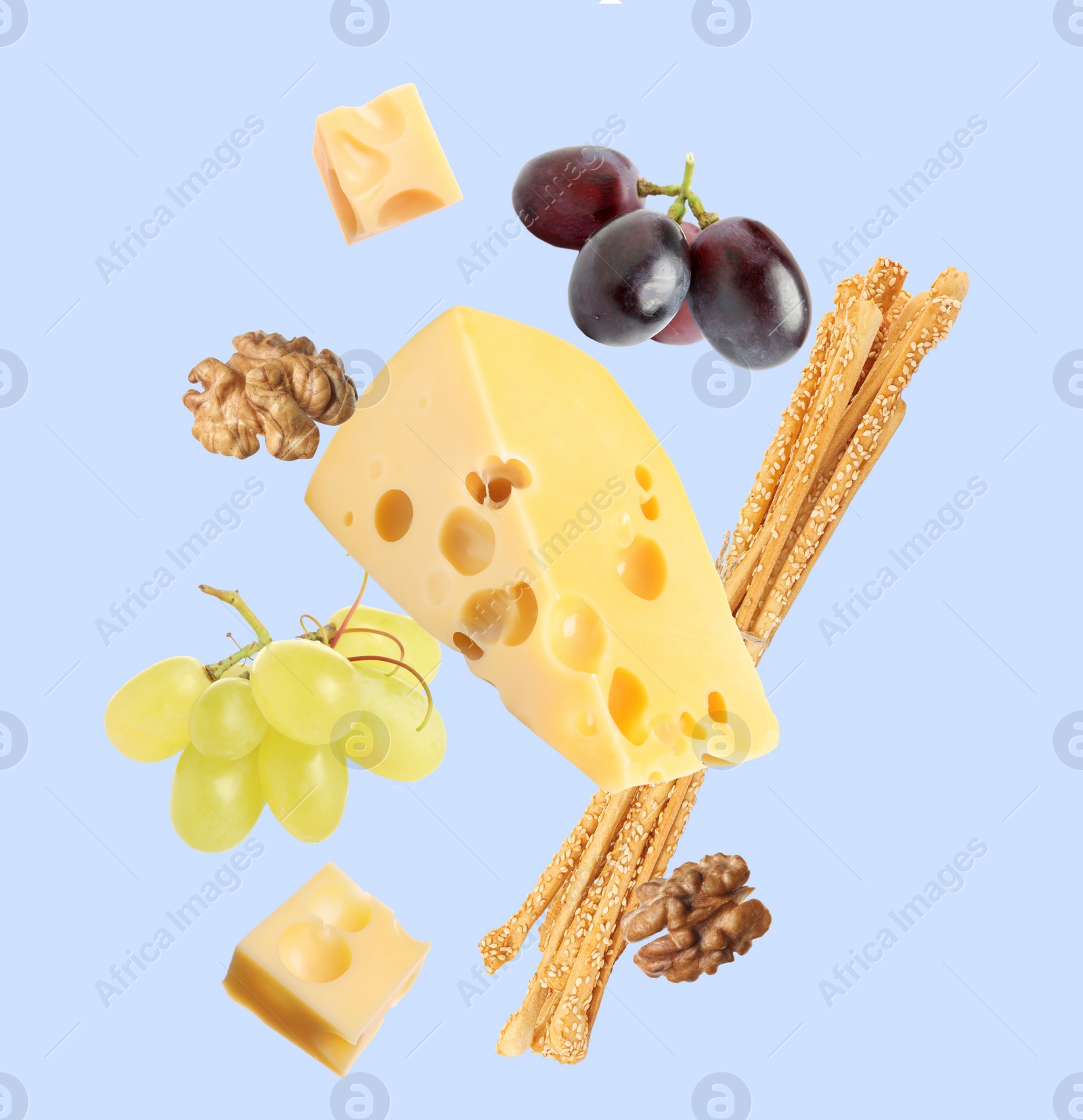 Image of Cheese, breadsticks, grapes and walnuts falling against pale light blue background