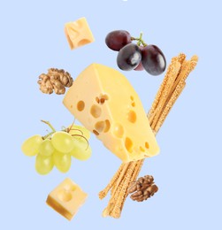 Image of Cheese, breadsticks, grapes and walnuts falling against pale light blue background