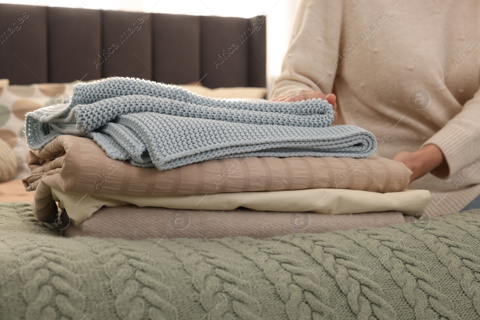Photo of Woman with stack of different folded blankets on bed, closeup. Home textile