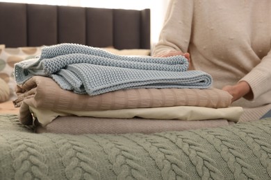 Woman with stack of different folded blankets on bed, closeup. Home textile