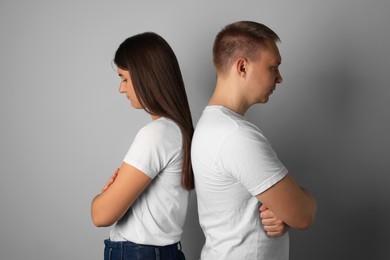 Photo of Unhappy young couple turning their backs on each other against light background