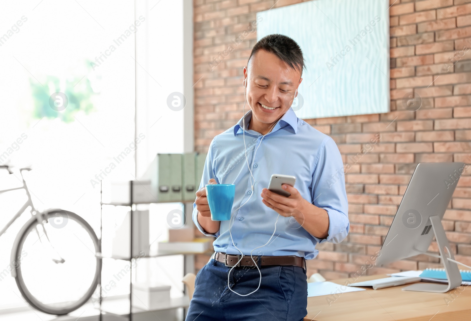 Photo of Happy young businessman with mobile phone listening to music in office. Peaceful moment