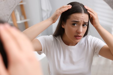 Photo of Emotional woman examining her hair and scalp at home. Dandruff problem