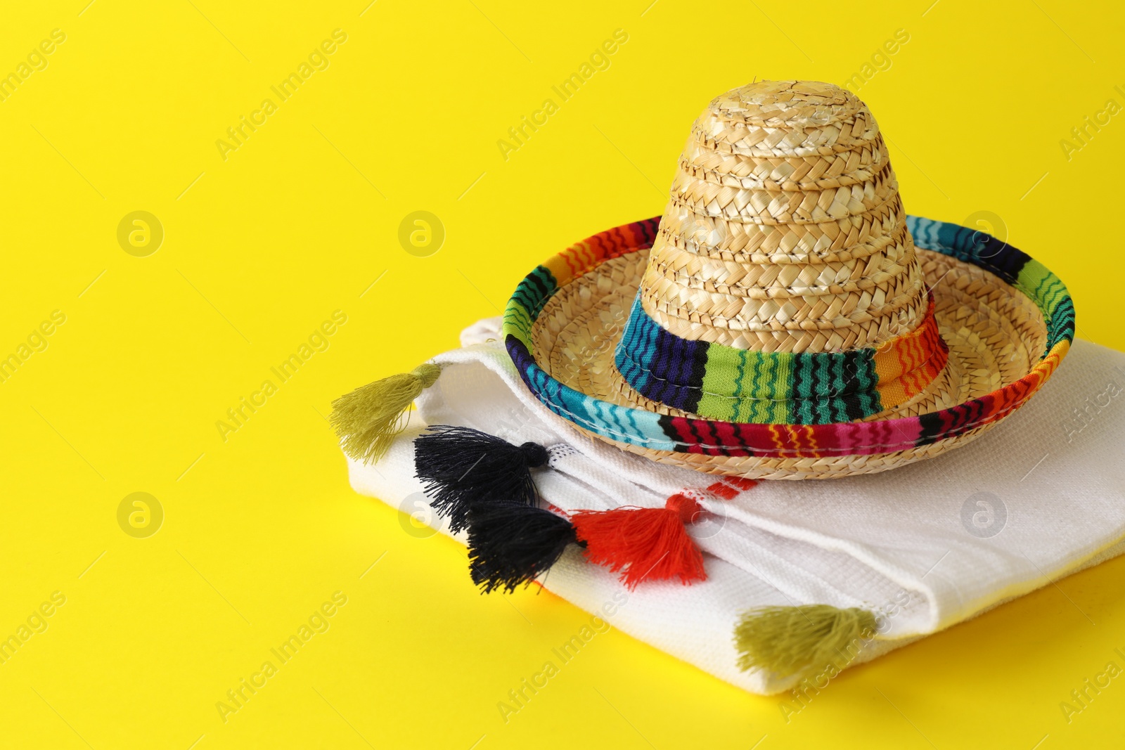 Photo of Mexican sombrero hat and poncho on yellow background, space for text