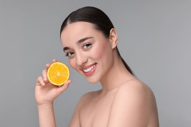 Beautiful young woman with piece of orange on grey background