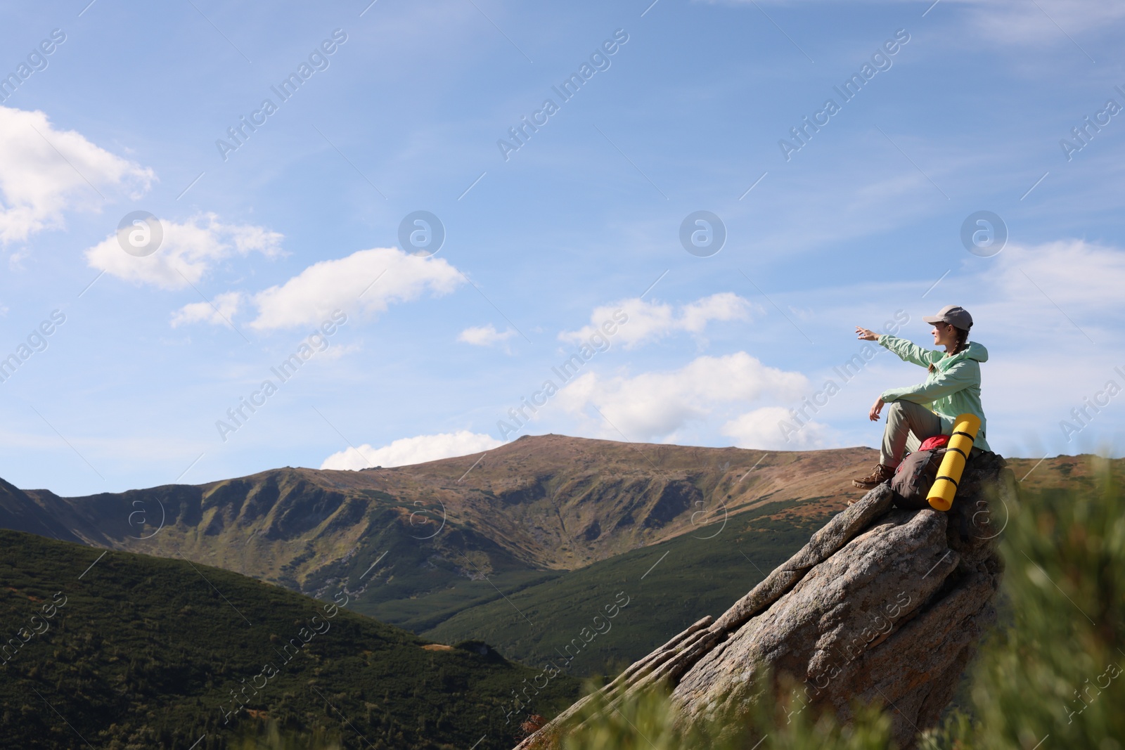 Photo of Young woman with backpack on rocky peak in mountains. Space for text