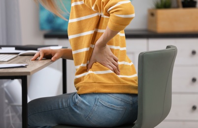 Photo of Young woman suffering from back pain in office, closeup