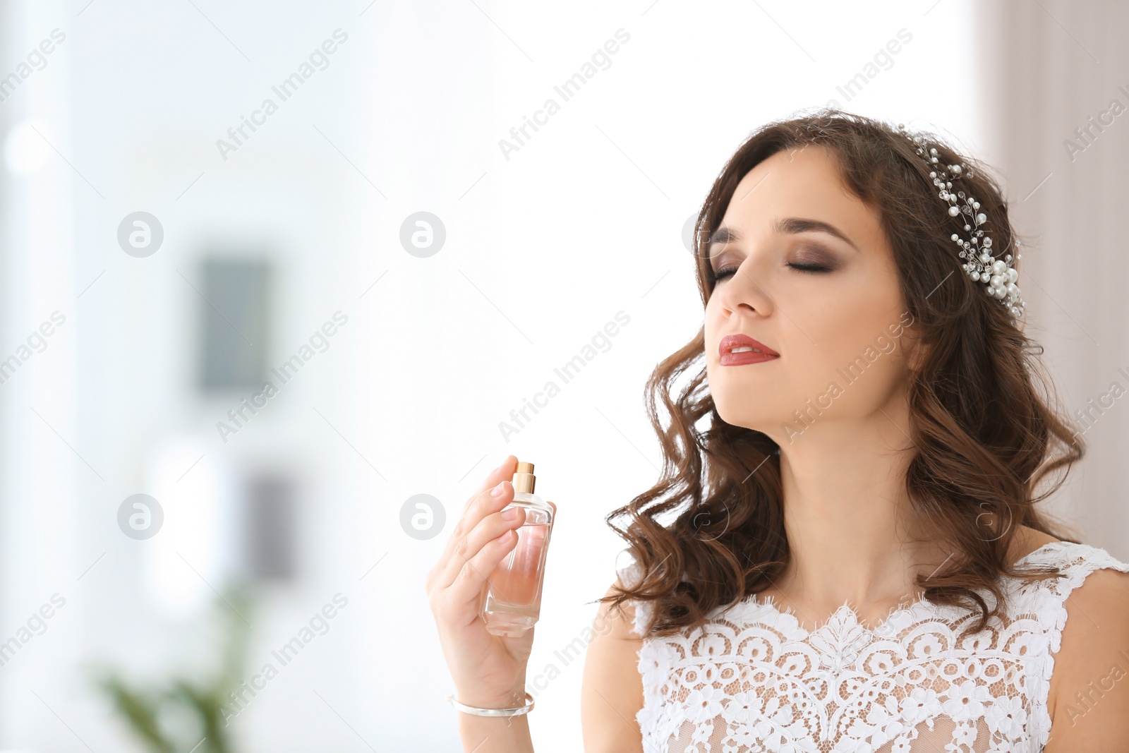 Photo of Beautiful young bride with bottle of perfume on blurred background