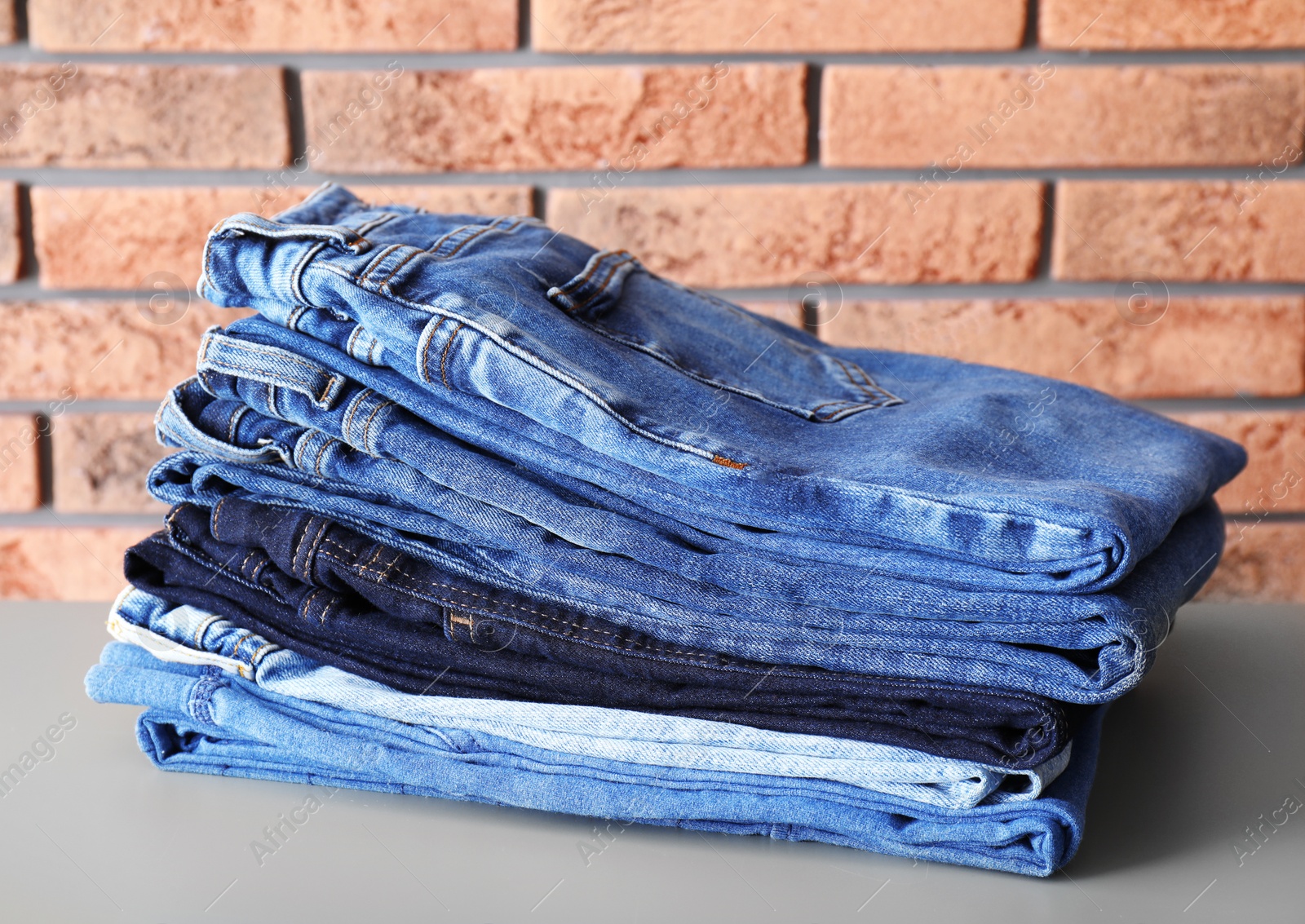 Photo of Stack of jeans on table against brick wall background