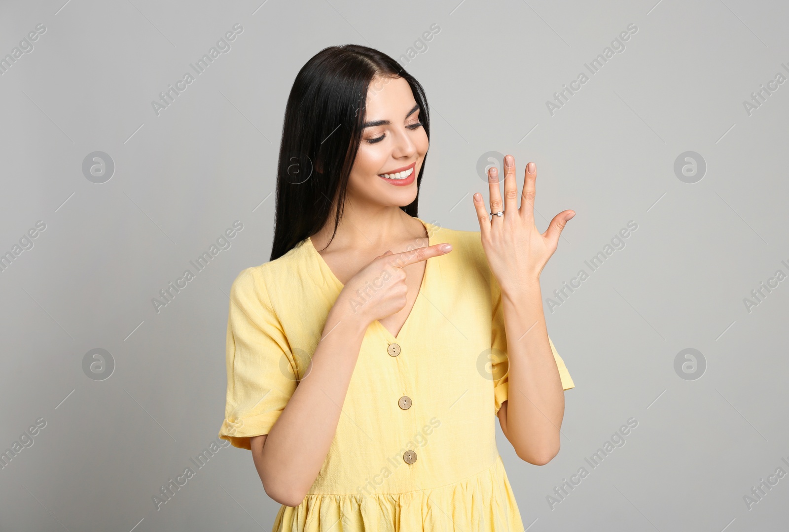 Photo of Happy young woman wearing beautiful engagement ring on grey background