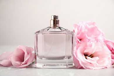 Photo of Bottle of perfume with fresh flowers on light background