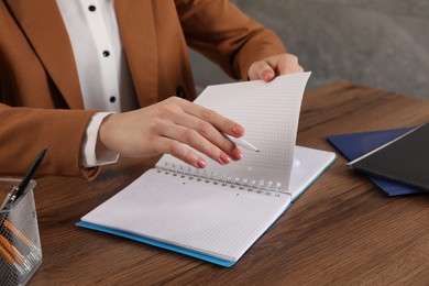 Photo of Woman taking notes at wooden table indoors, closeup