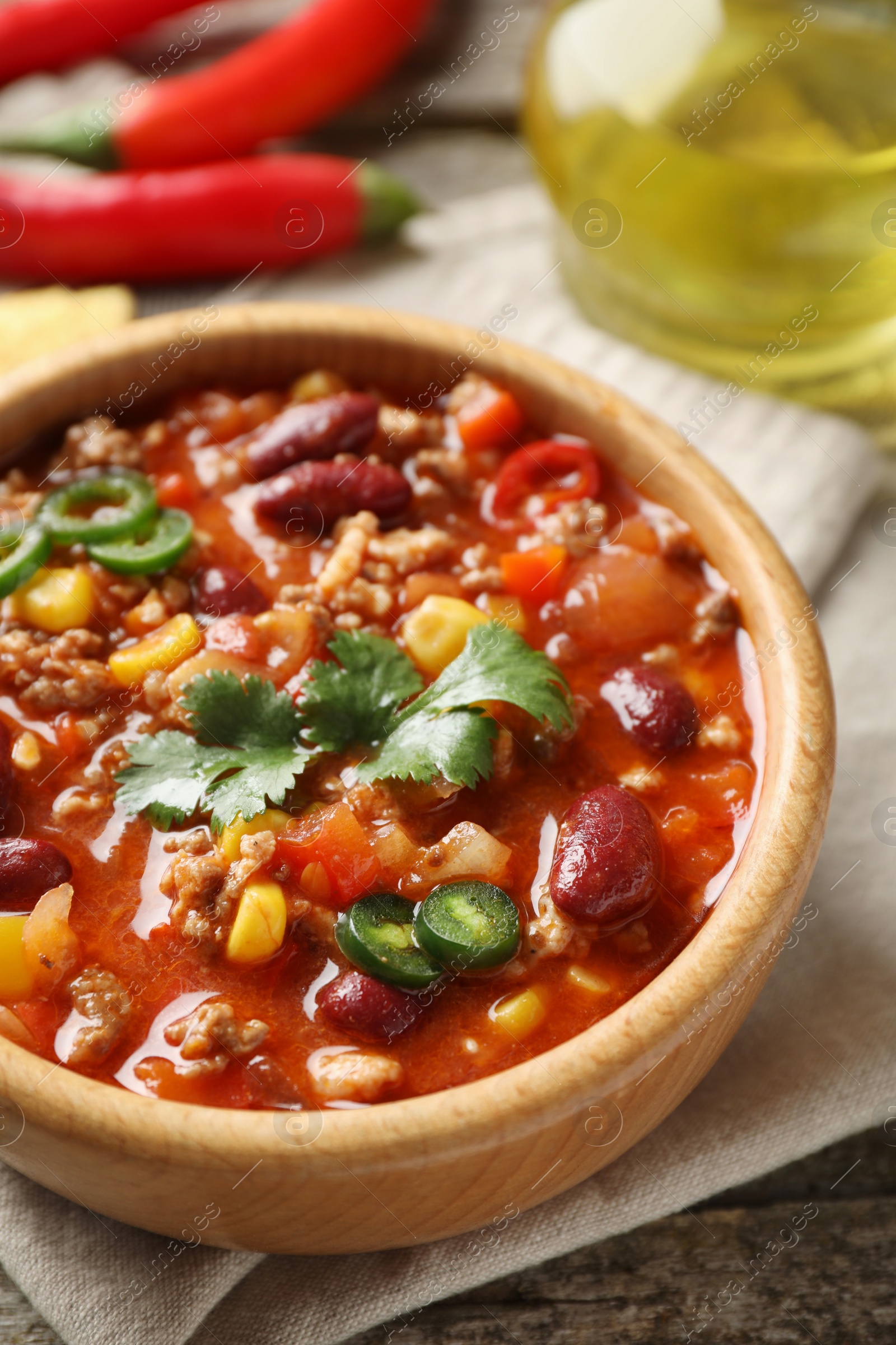 Photo of Bowl with tasty chili con carne on wooden table, closeup