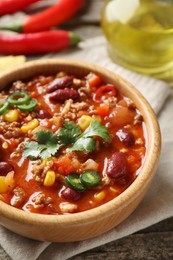 Bowl with tasty chili con carne on wooden table, closeup