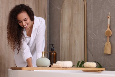 Beautiful African American woman near tub in bathroom, space for text