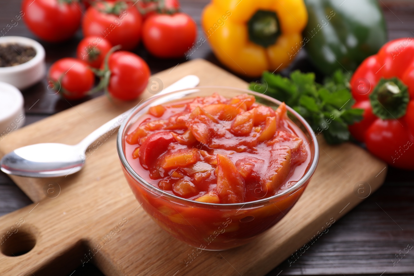 Photo of Delicious lecho in bowl and fresh ingredients on wooden table, closeup