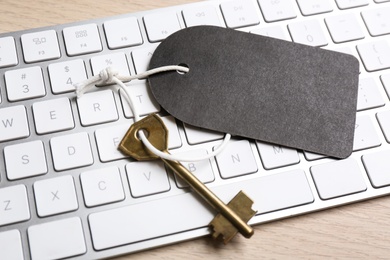 Key with blank tag and computer keyboard on table, closeup. Keyword concept