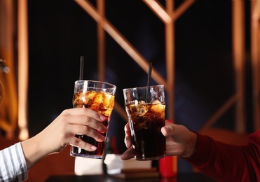 Photo of Young couple with glasses of refreshing cola at table indoors, closeup