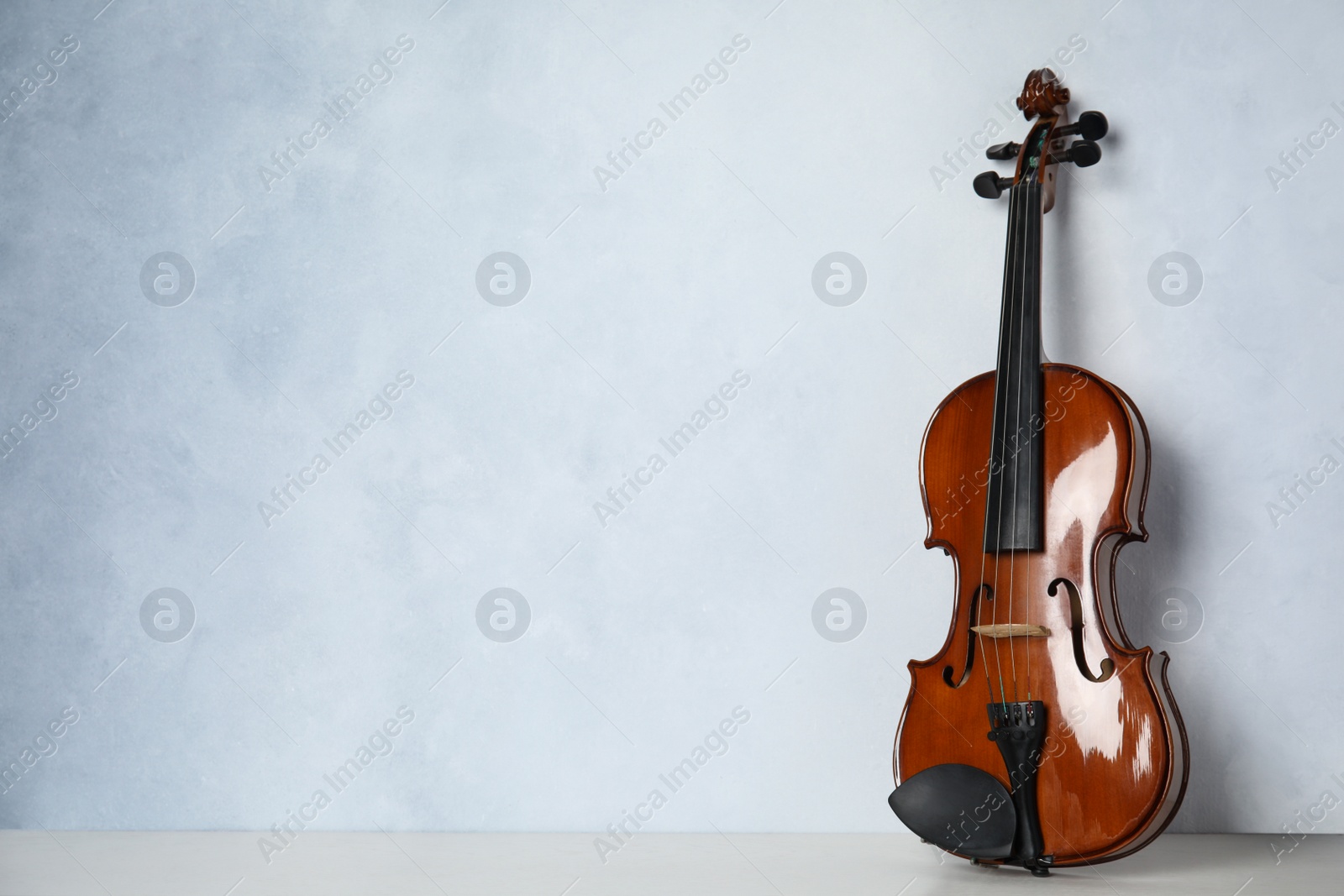 Photo of Beautiful violin on table near light blue wall. Space for text