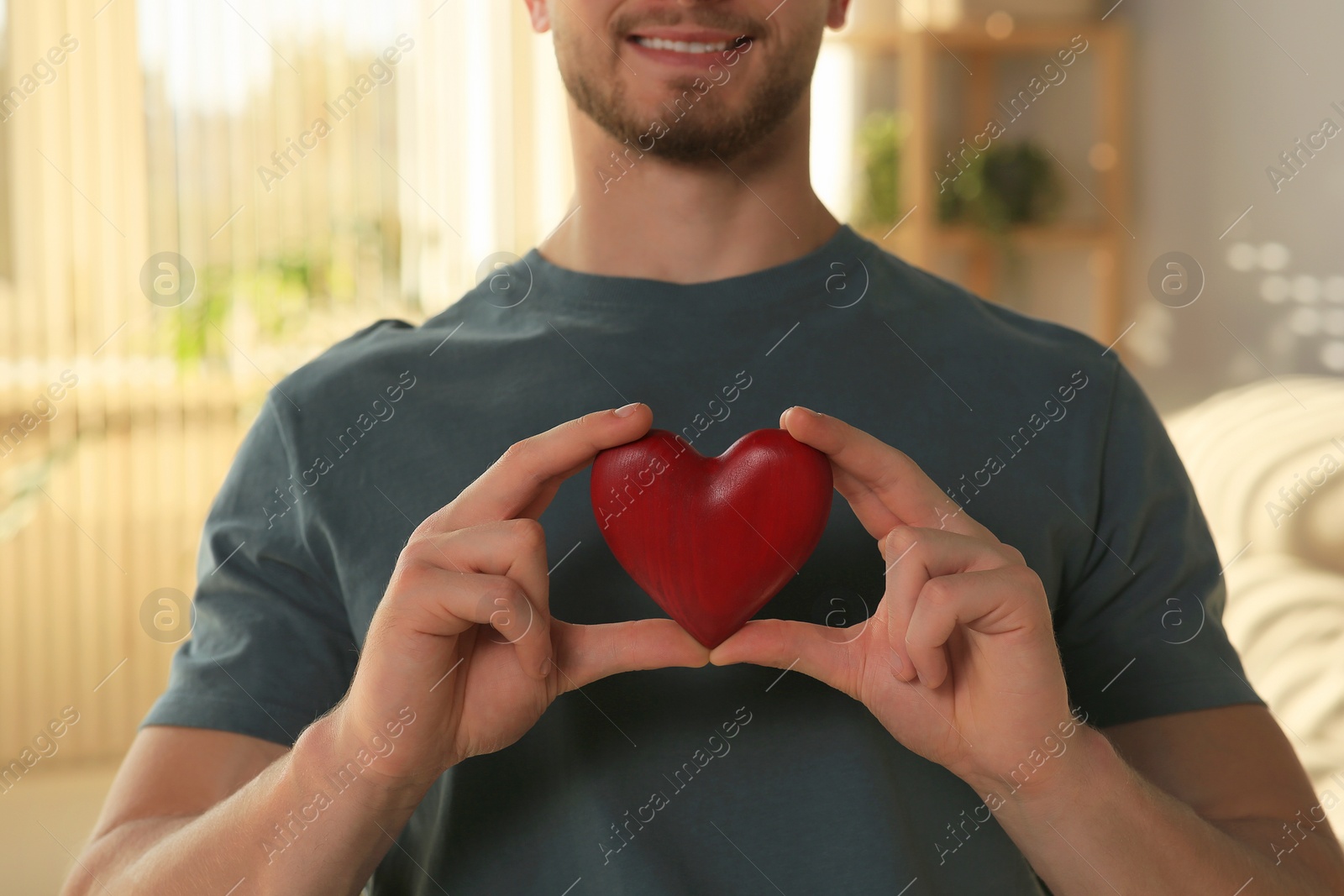 Photo of Happy volunteer holding red heart with hands indoors, closeup