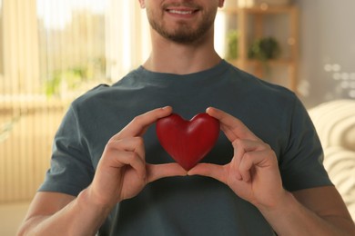 Happy volunteer holding red heart with hands indoors, closeup