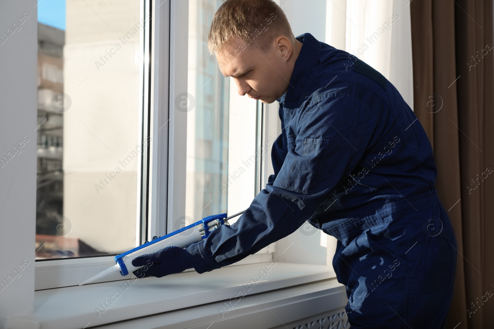 Photo of Construction worker sealing window with caulk indoors