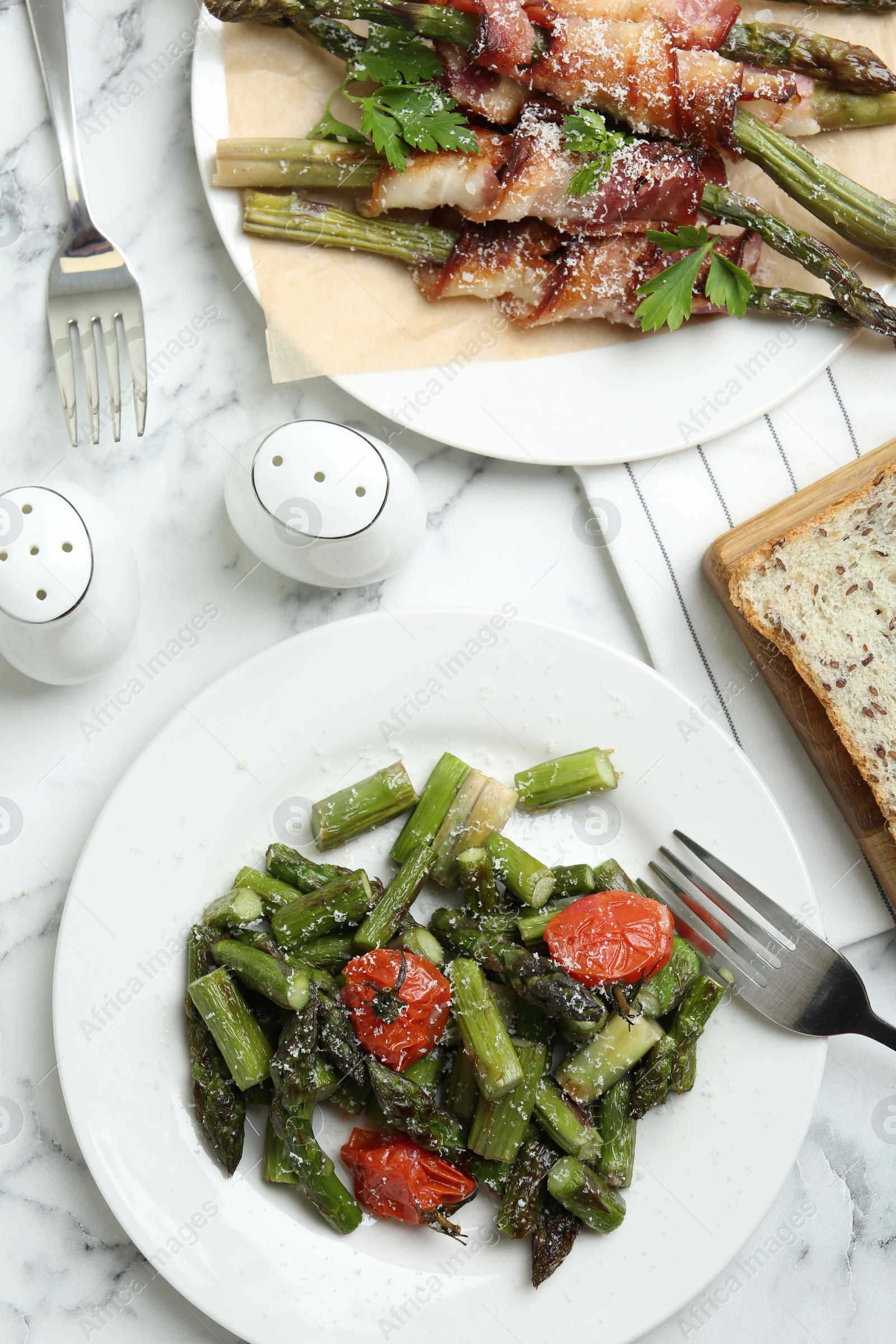 Photo of Dishes with oven baked asparagus served on white marble table, flat lay