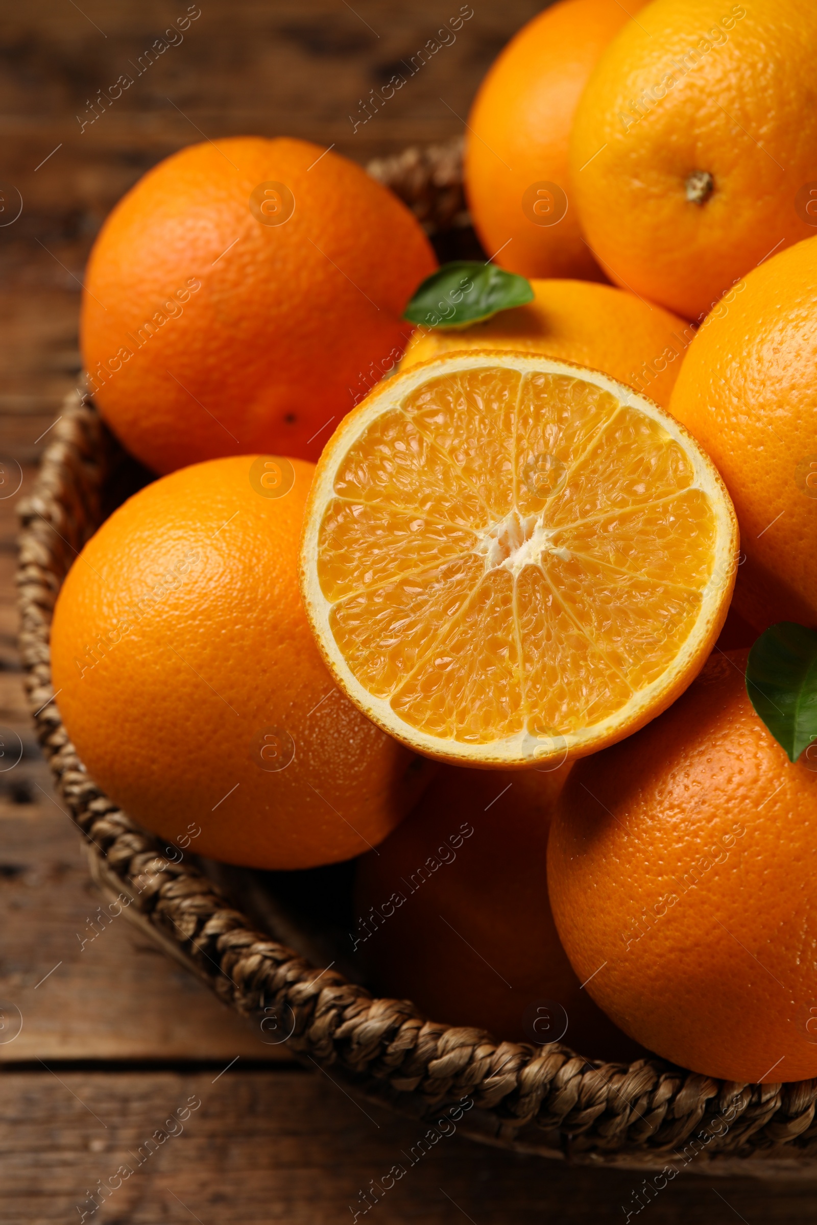 Photo of Many ripe oranges and green leaves on wooden table, closeup