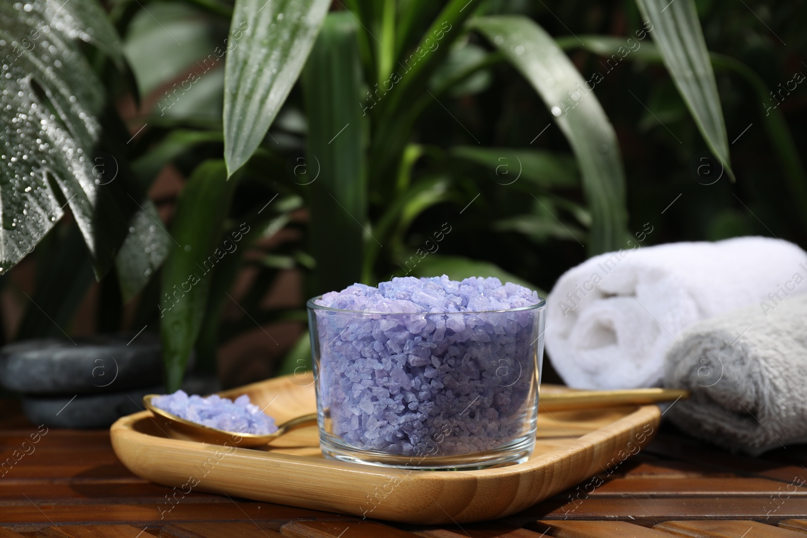 Photo of Bowl of purple sea salt, spoon and rolled towels on wooden table, closeup