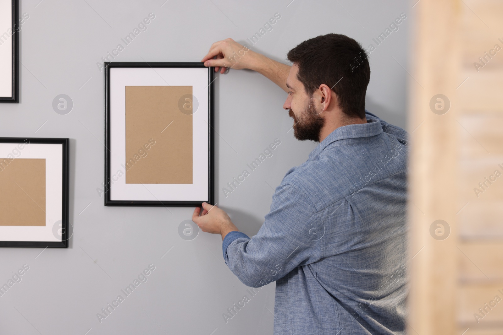 Photo of Man hanging picture frame on gray wall indoors