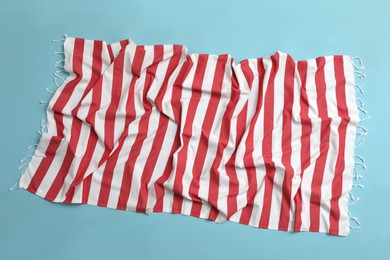 Photo of Crumpled striped beach towel on light blue background, top view