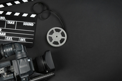 Photo of Modern video camera, movie clapper and reel on black background, flat lay. Space for text