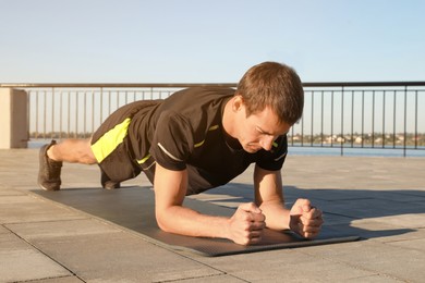 Photo of Sporty man doing plank exercise on mat outdoors