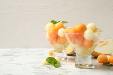 Photo of Melon balls and mint on white marble table, space for text