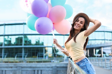 Photo of Beautiful young woman with color balloons on city street