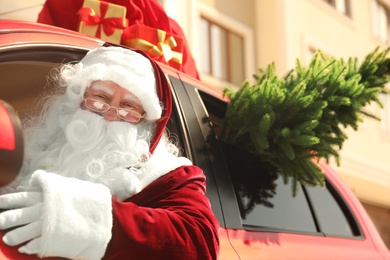 Photo of Authentic Santa Claus with fir tree and bag full of presents on roof driving modern car, outdoors