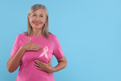 Photo of Senior woman with pink ribbon on light blue background, space for text. Breast cancer awareness