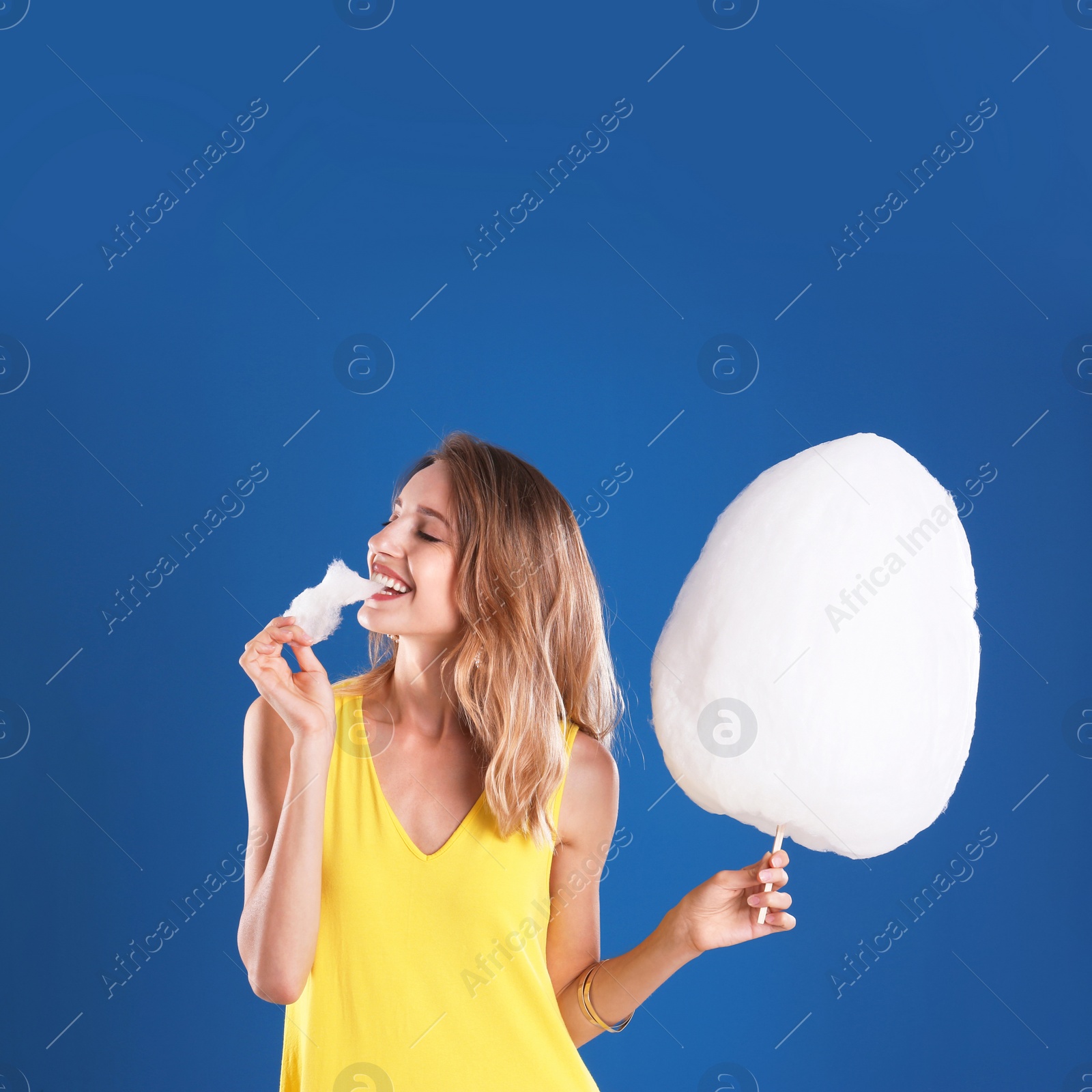 Photo of Happy young woman eating cotton candy on blue background
