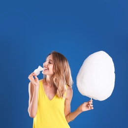 Photo of Happy young woman eating cotton candy on blue background