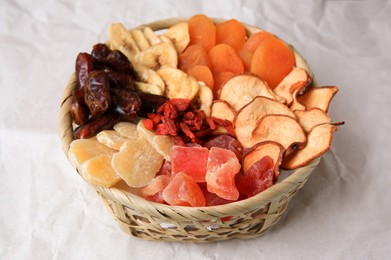 Photo of Wicker basket with different dried fruits on paper