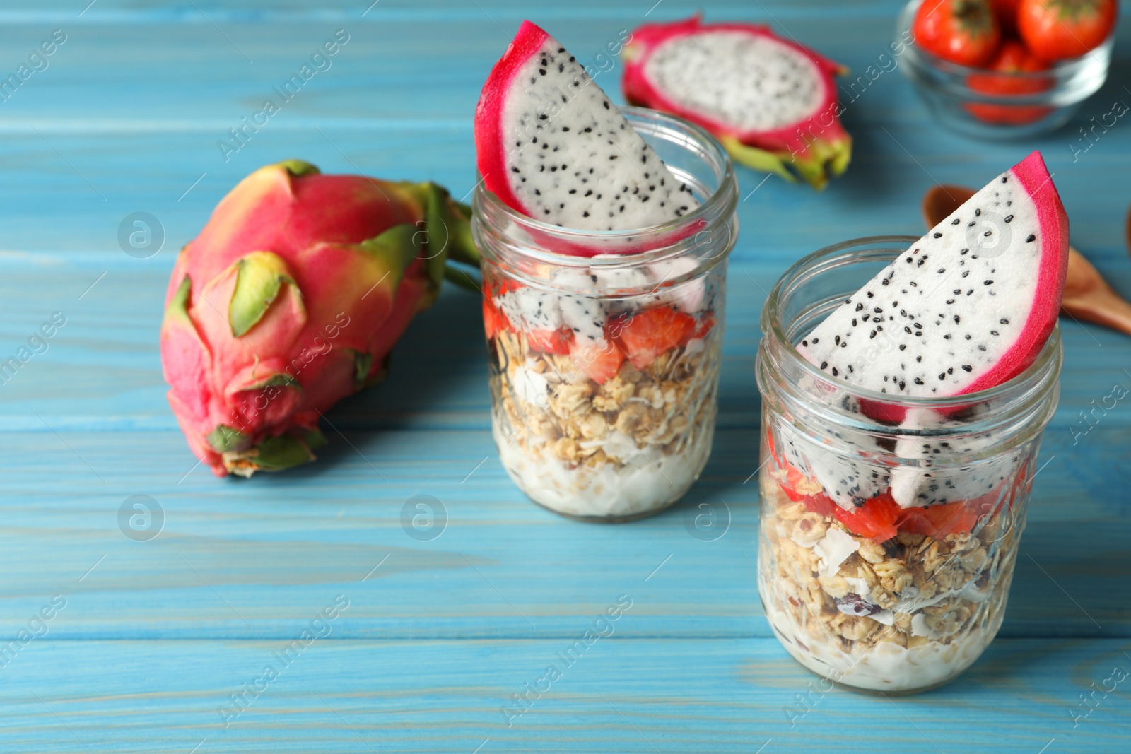 Photo of Granola with strawberries and pitahaya in glass jars on  light blue wooden table