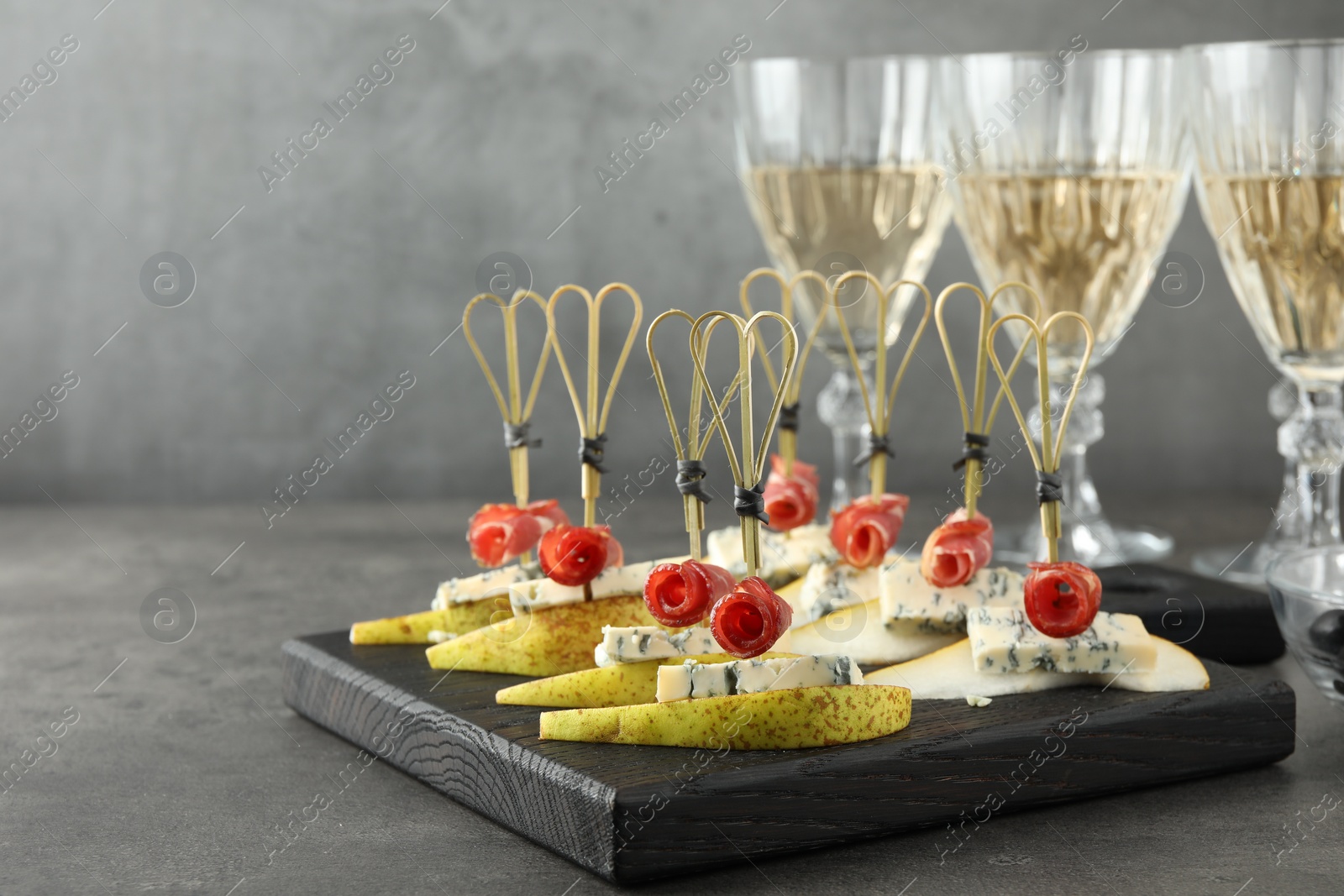 Photo of Tasty canapes with pears, blue cheese and prosciutto on grey table, closeup. Space for text