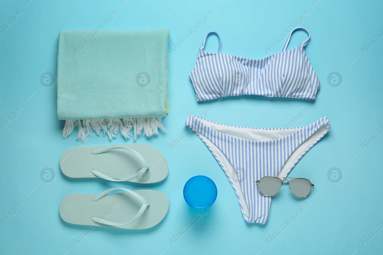 Photo of Beach towel, swimsuit, flip flops and sunglasses on light blue background, flat lay