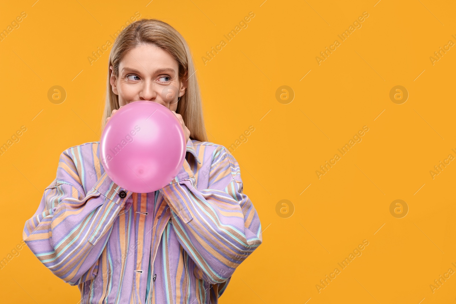 Photo of Woman blowing up balloon on yellow background. Space for text