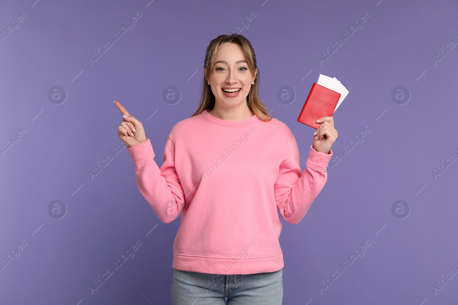 Photo of Happy young woman with passport and ticket pointing at something on purple background